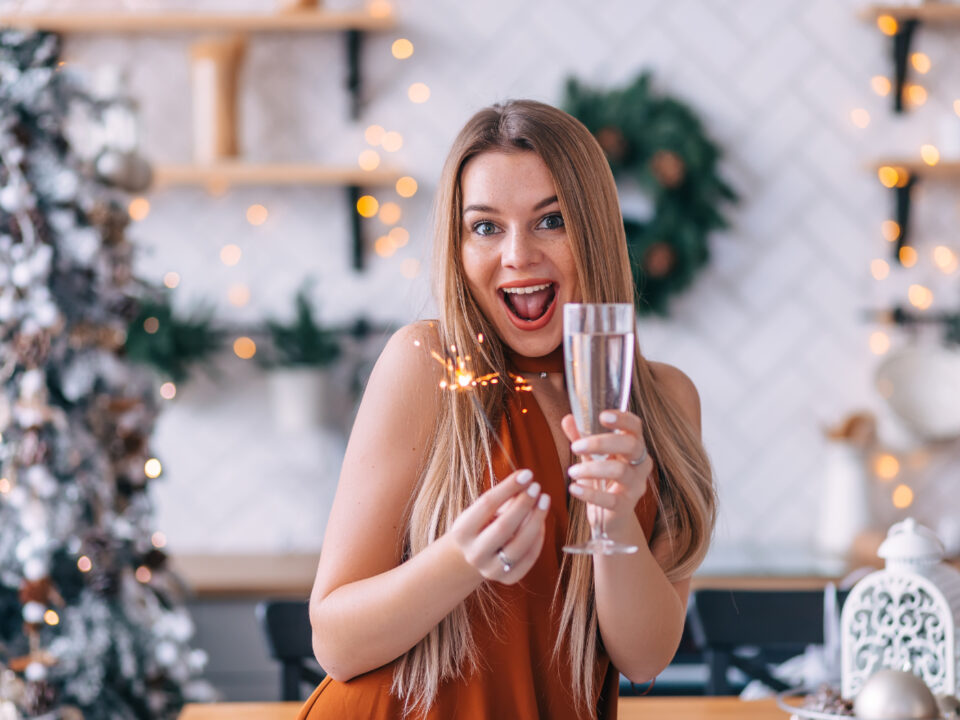 mulher com uma taça de champanhe na mão comemorando em um ambiente natalino