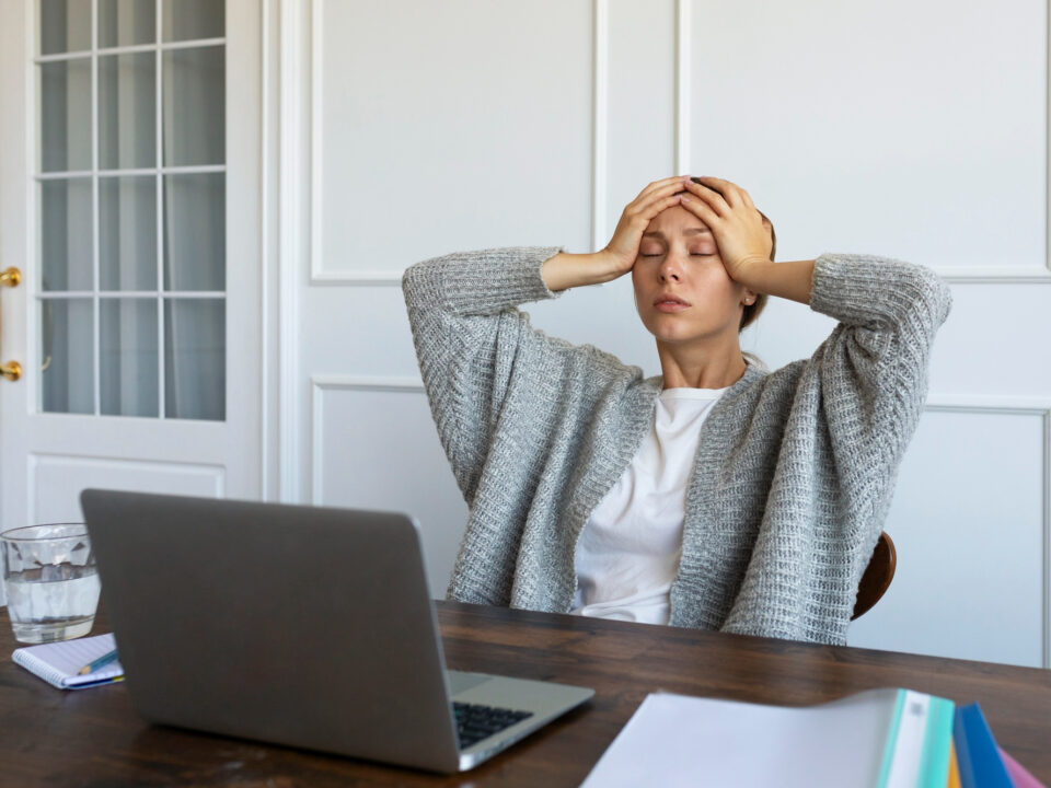 Moça sentada em frente ao computador com as mãos na cabeça, parecendo preocupada