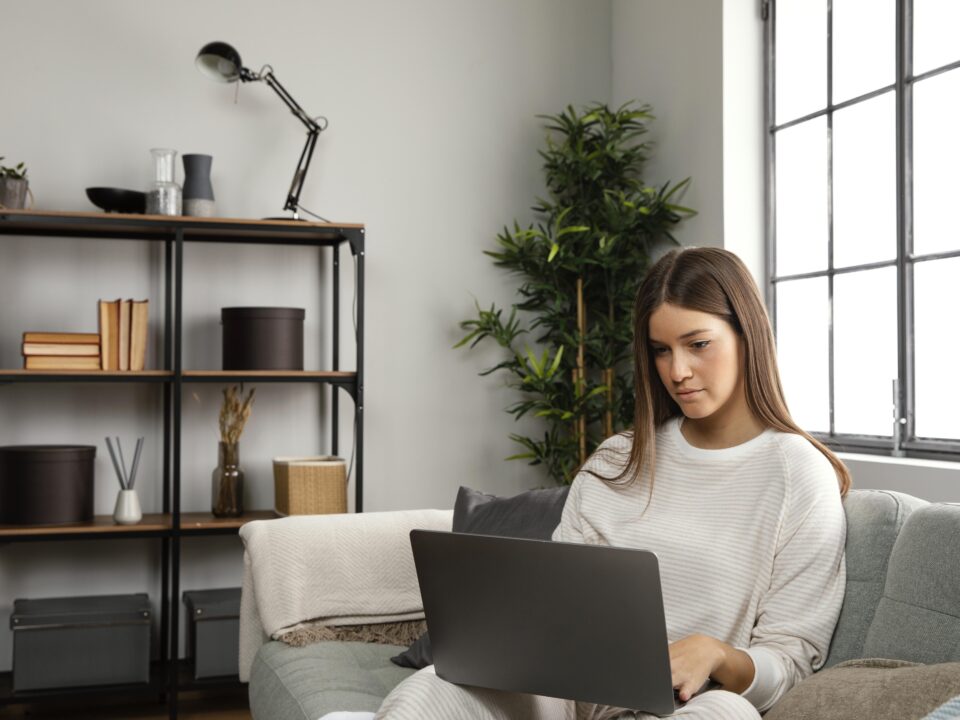 mulher sentada no sofa com um computador em mãos trabalhando home office