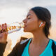 mulher com fone de ouvido ao ar livre tomando água em uma garrafa de vidro