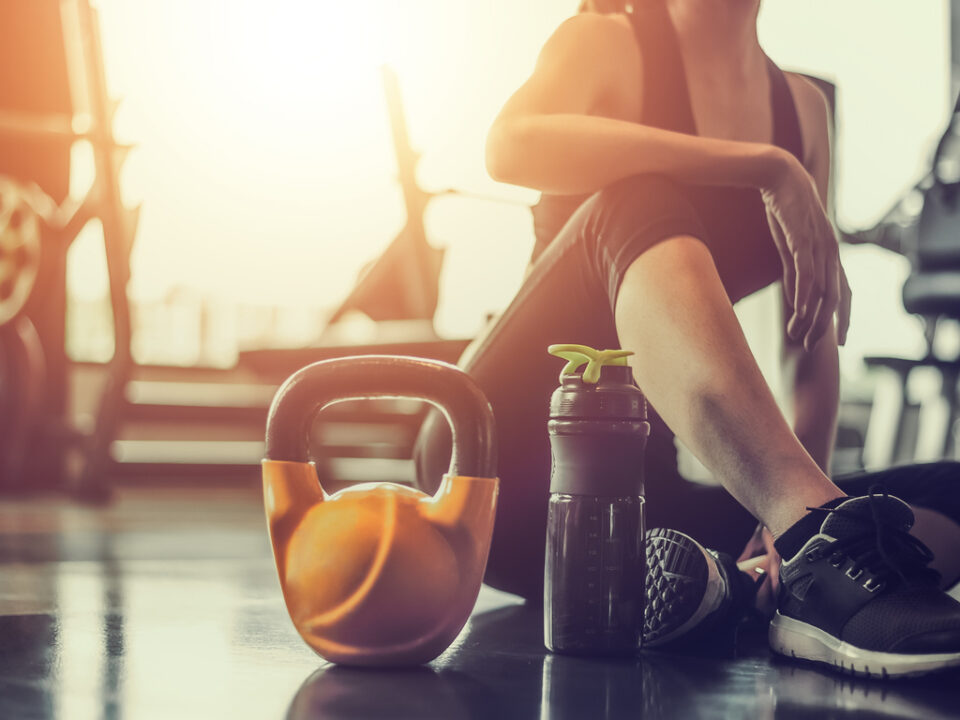 moça sentada na academia com um peso e uma garrafa de água na frente