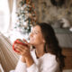 mulher serena sentada em uma rede e tomando alguma bebida em uma caneca, com ambiente de natal ao fundo