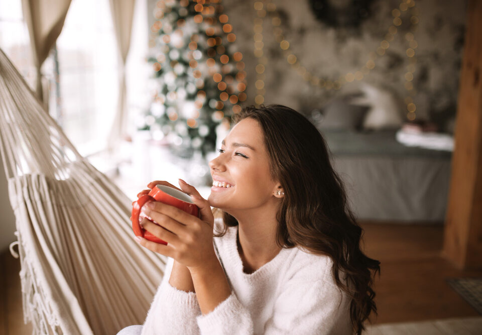 mulher serena sentada em uma rede e tomando alguma bebida em uma caneca, com ambiente de natal ao fundo
