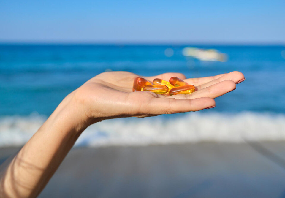 Mão com fundo de praia segurando suplementos em cápsulas